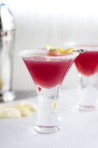 cranberry raspberry lemon drops in short martini glasses with lemon peel and a cocktail shaker in background