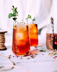 2 rose cardomom bourbon cocktails with ice and herbs and rose petals