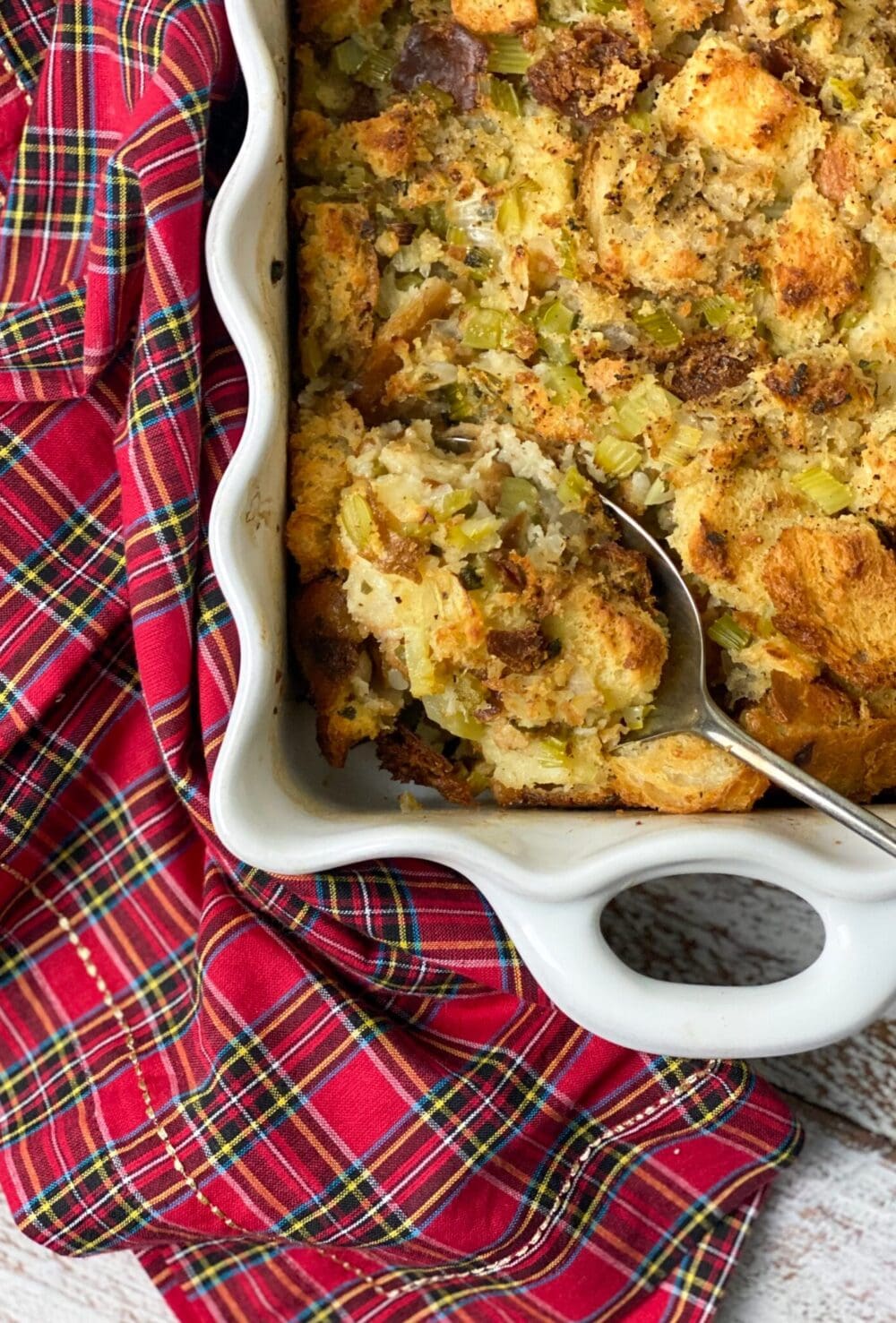 Old fashioned Thanksgiving dressing in a white pan with a spoon and a plaid napkin