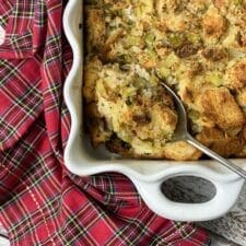 Old fashioned Thanksgiving dressing in a white pan with a spoon and a plaid napkin