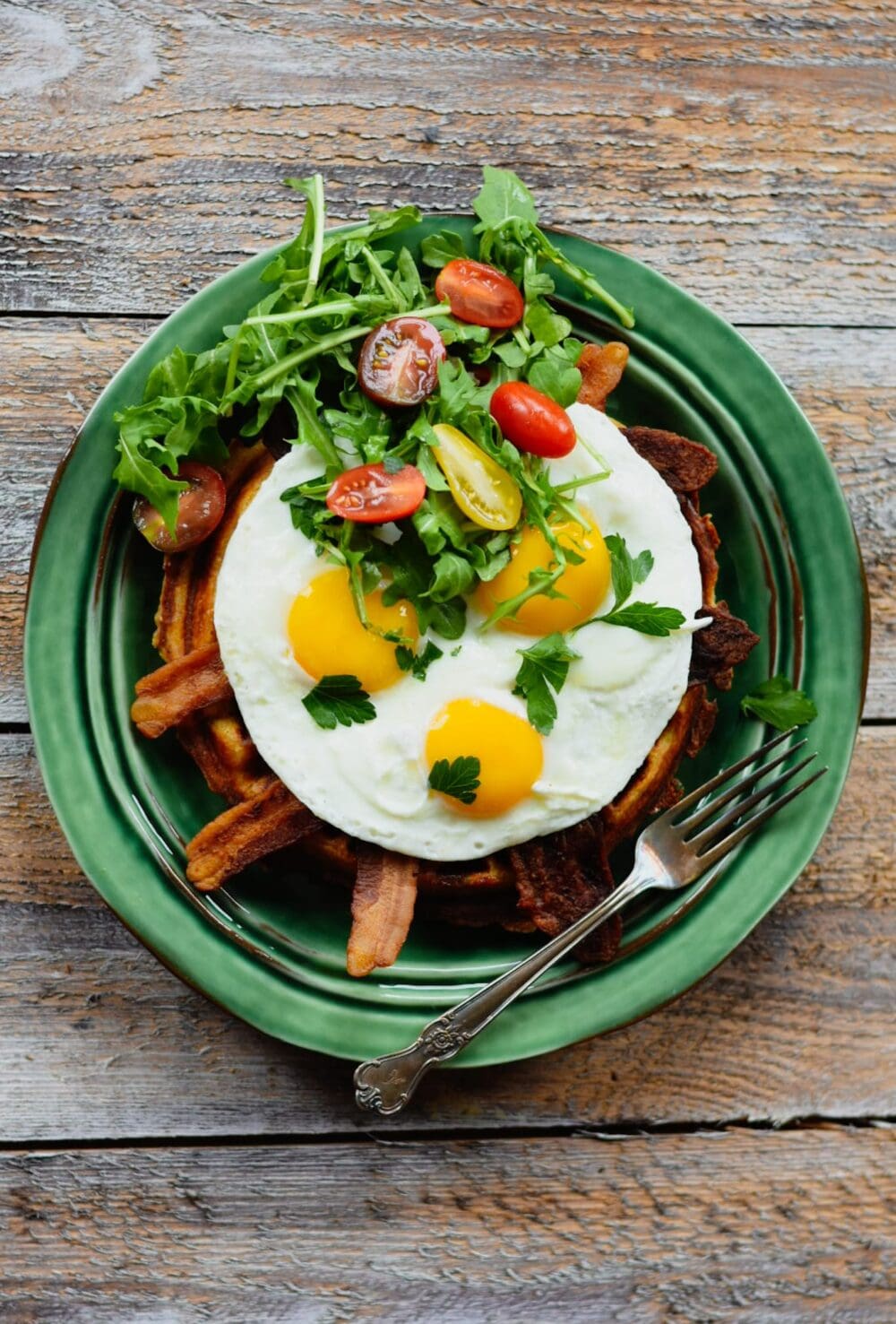 Waffle, bacon, eggs, tomato and arugula on a green plate