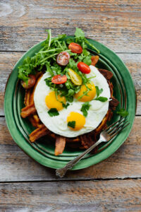 Waffle, bacon, eggs, tomato and arugula on a green plate