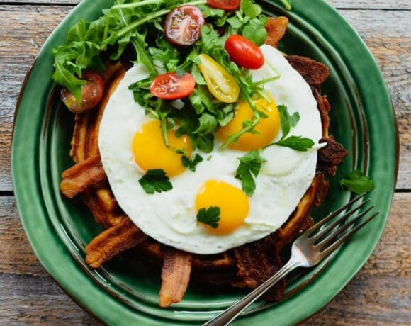 Waffle, bacon, eggs, tomato and arugula on a green plate