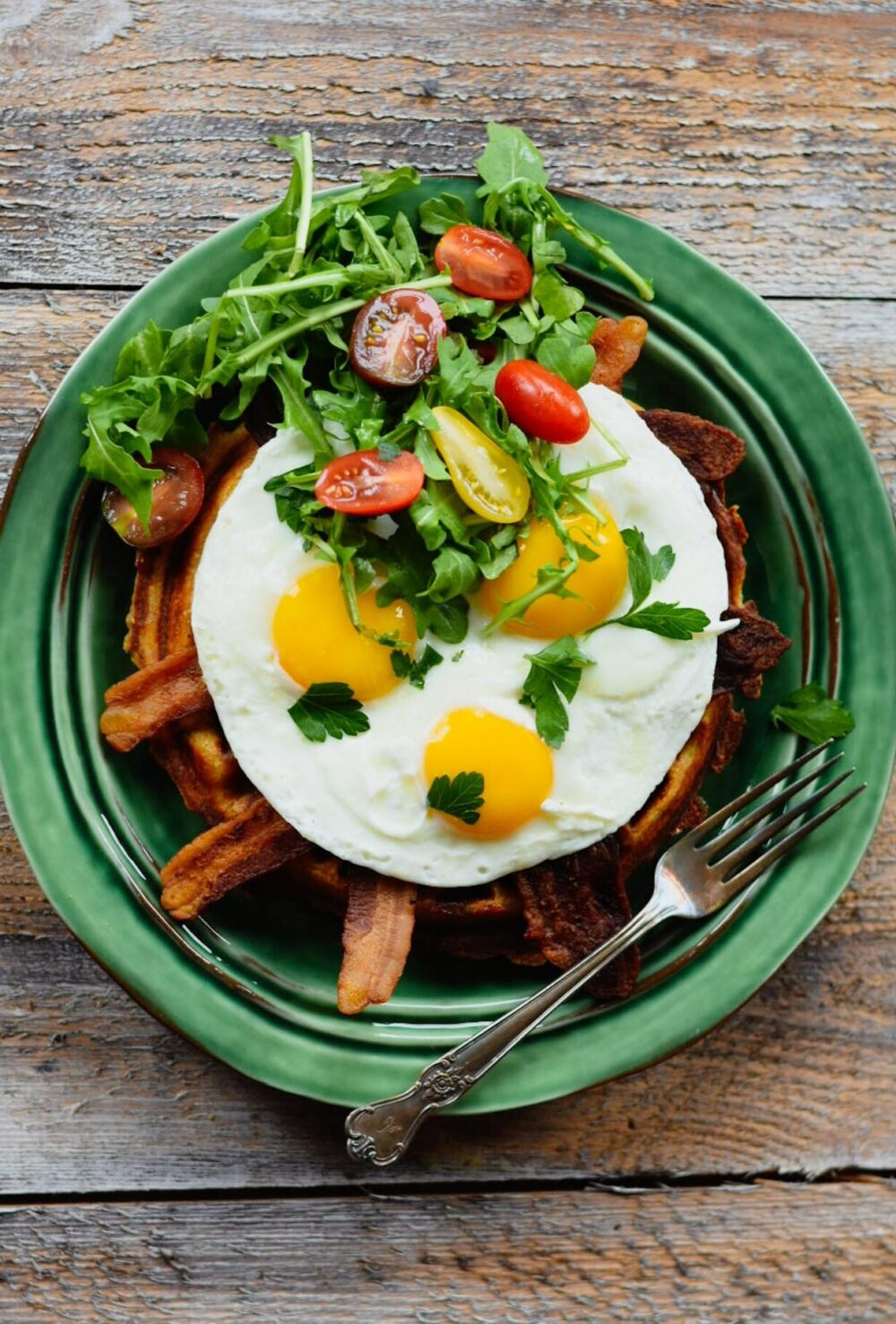 Waffle, bacon, eggs, tomato and arugula on a green plate