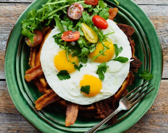 Waffle, bacon, eggs, tomato and arugula on a green plate
