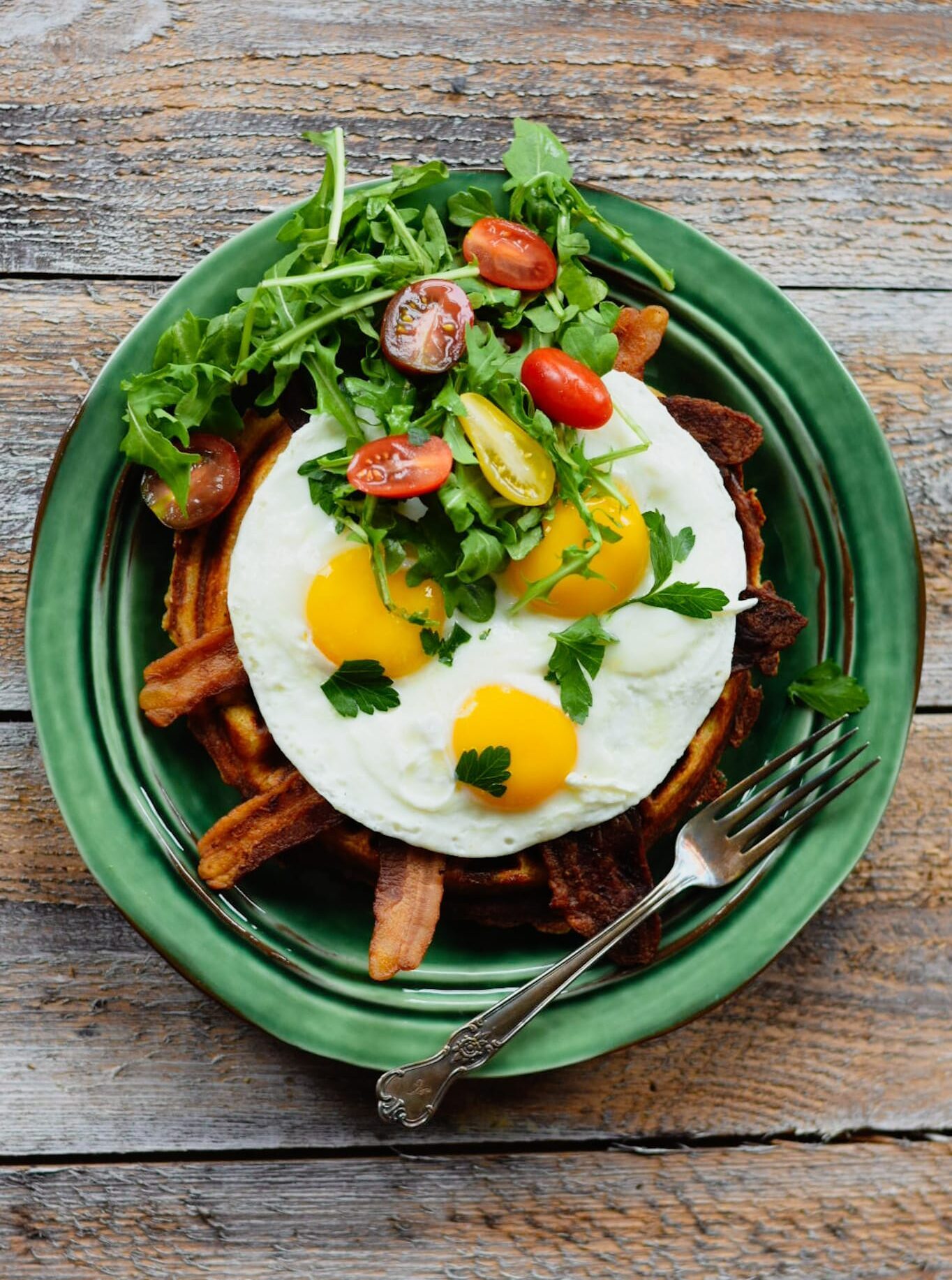 Waffle, bacon, eggs, tomato and arugula on a green plate