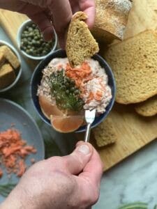 Smoked salmon spread and capers getting put on a piece of bread