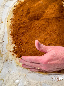 hand adding cinnamon and brown sugar to dough