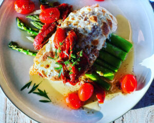 Italian Chicken Cutlets topped with melty mozzarella cheese and a cherry tomato white wine sauce on top of asparagus
