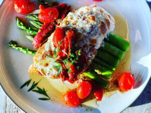 Italian Chicken Cutlets topped with melty mozzarella cheese and a cherry tomato white wine sauce on top of asparagus