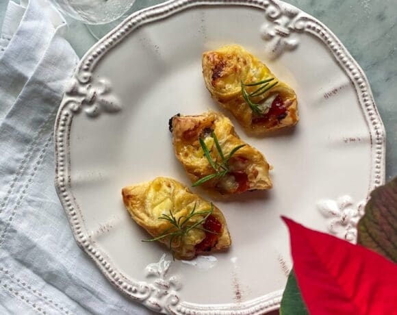3 puff pastry wrapped brie, prosciutto, and pepper jelly bites, with a glass of champagne, with cranberries, and a poinsettia