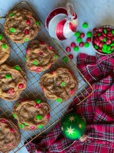 m&m chocolate chip cookies in stacks on a cooking rack with a bowl of m&ms and some christmas ornaments