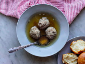 3 meatballs in broth with a plate of rolls