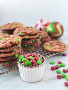 m&m chocolate chip cookies in stacks on a cooking rack with a bowl of m&ms and some christmas ornaments