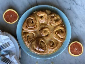 a plate of orange rolls and 2 oranges