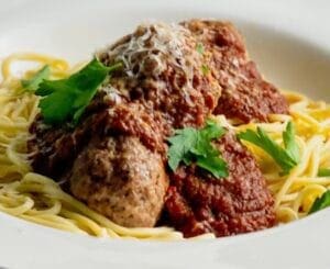 Tomato sauce over meatballs and pasta with parsley