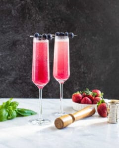 2 blueberry basil french 75 cocktails with a bowl of strawberries