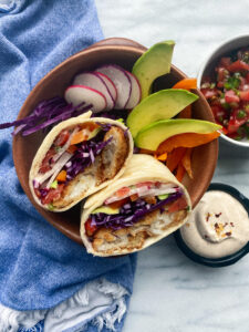 Baja fish burrito in bowl with purple cabbage, radishes, avocado and peppers with baja sauce and pico di gallo on side