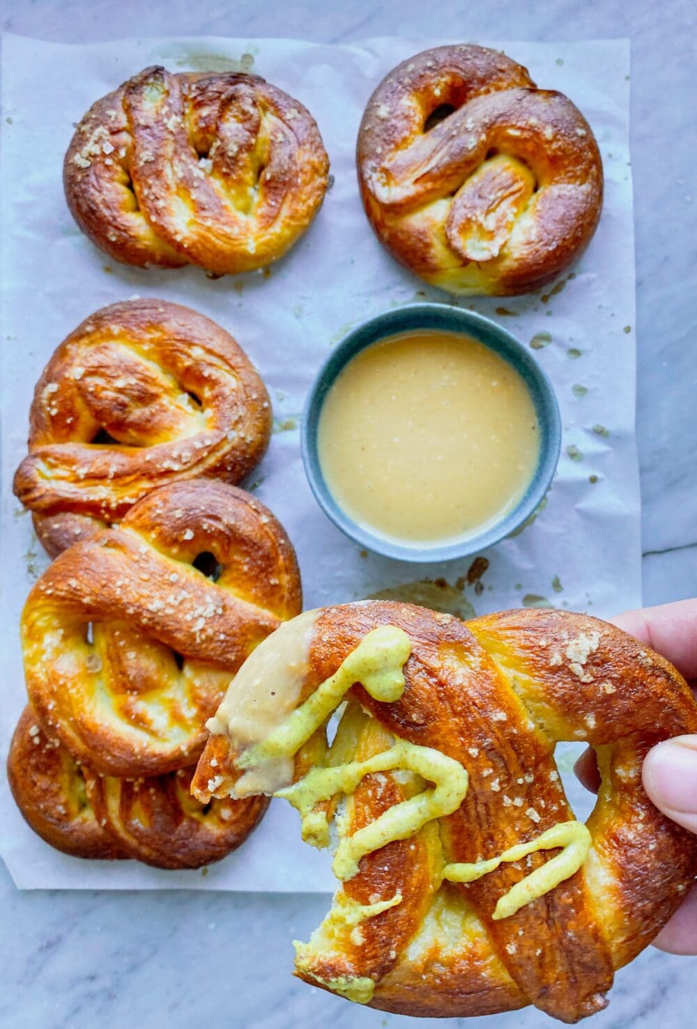 5 soft pretzels and cheese sauce and one pretzel with mustard and a bite taken out of it being held by a hand