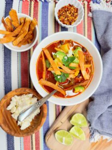 Tortilla chicken soup with avocado, cheese and limes and tortilla strips and hot pepper flackes