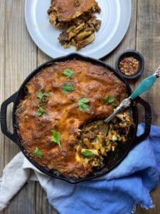 Italiian Sausage PAsta bake in a cast iron pan with chili flakes in a little bowl and a plate with some of the past aon i