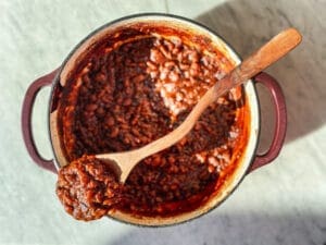 Homemade bbq baked beans in a cast iron dutch oven with a wooden spoon.