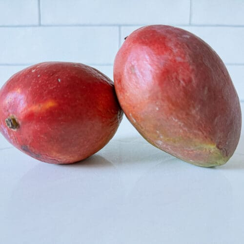 2 red skinned mangos on a counter
