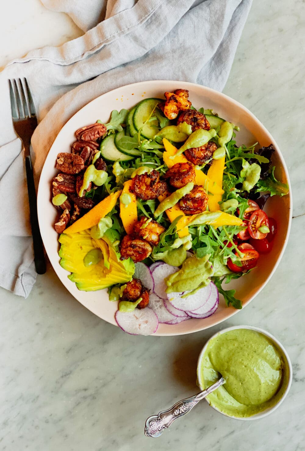fork and napkin and mango shrimp salad in a bowl with a side of dressing