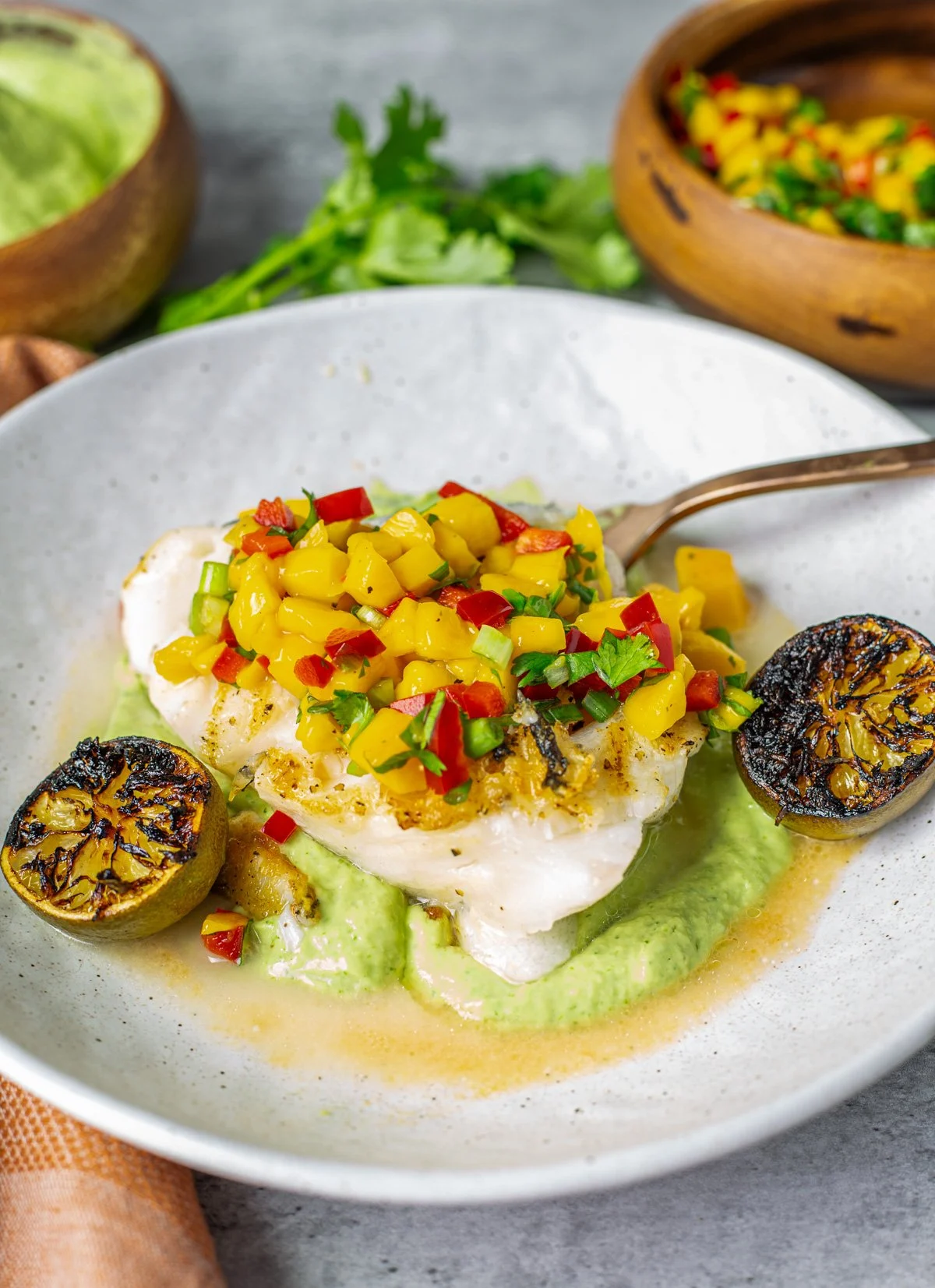 sea bass on a plate of gree sauce with grilled citrus and topped with mango salsa