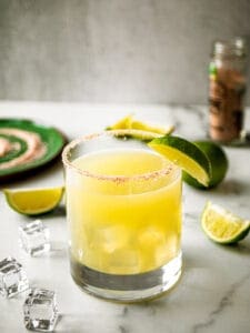 classic margarita in a glass with lime wedges and ice and salt plate next to it