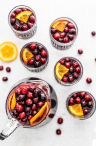 Cranberry orange red sangria in cups with a pitcher of sangria and cranberries and orange slices