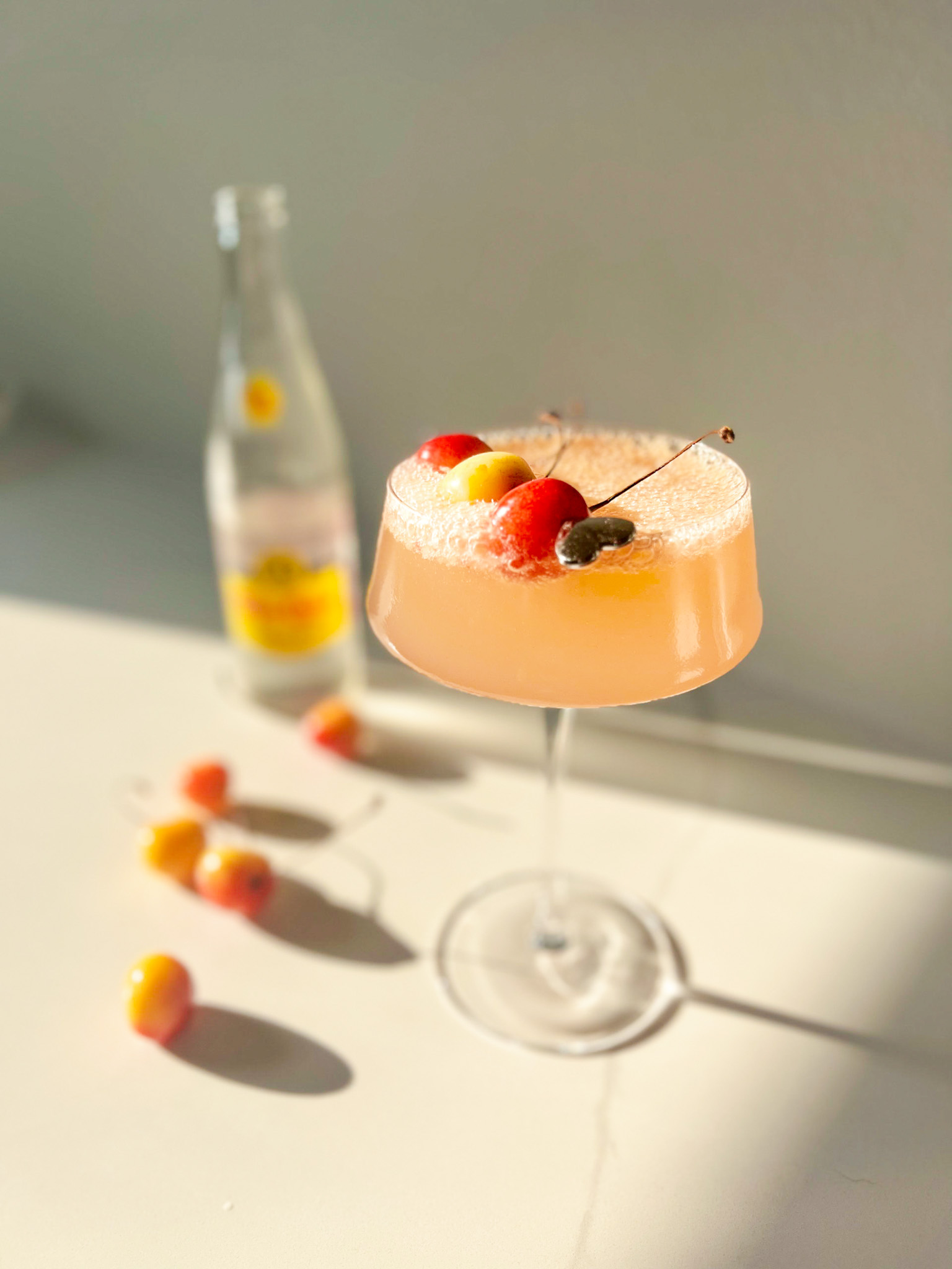 Mocktail version of a cherry sea breeze in a martini glass with a bottle of Topo Chico