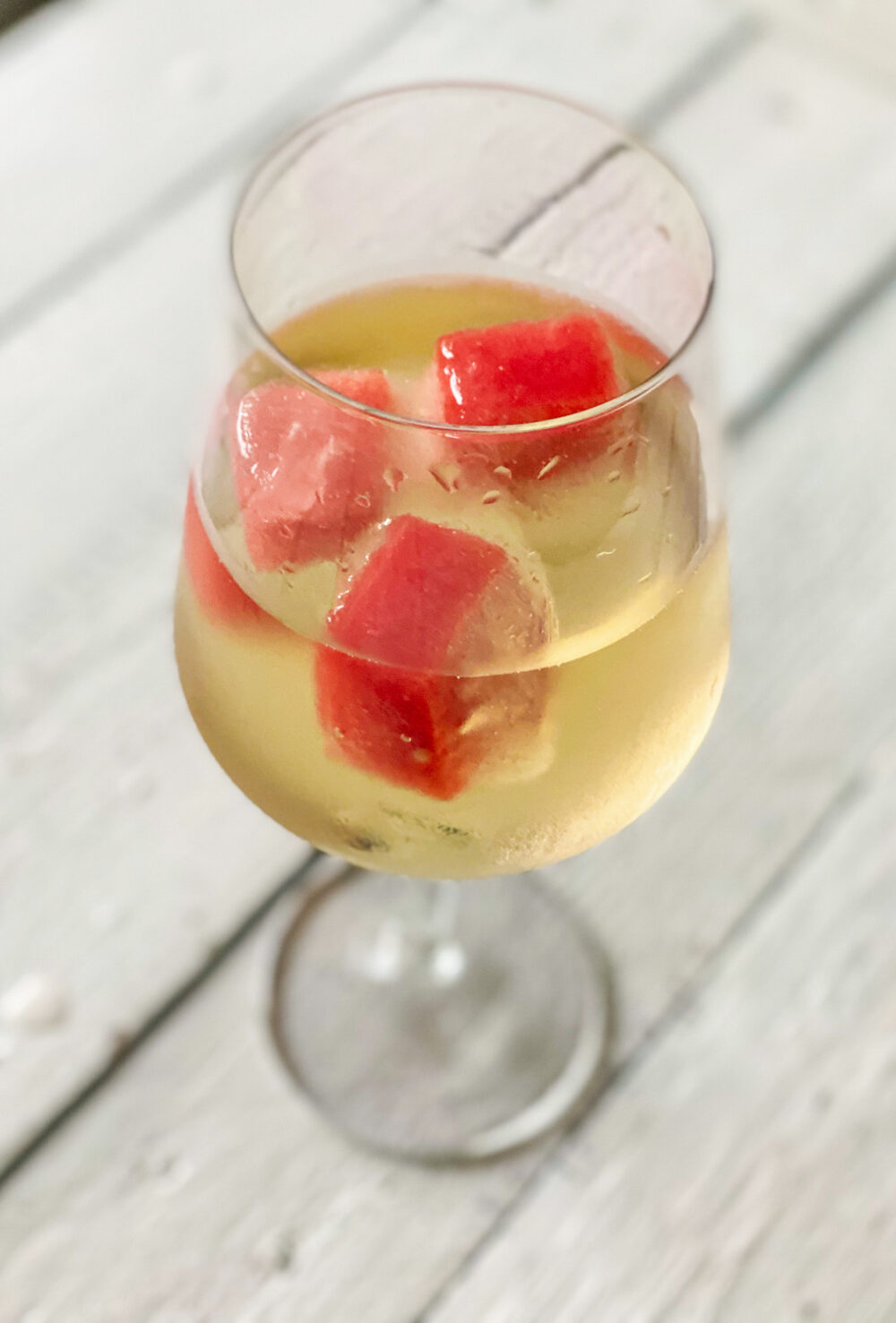 a glass of white wine with watermelon ice cubes