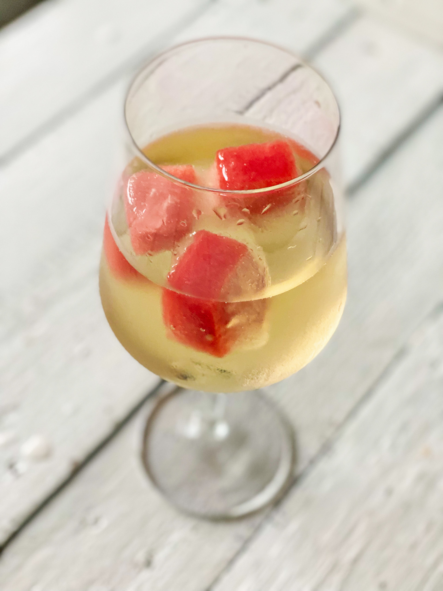 a glass of white wine with watermelon ice cubes