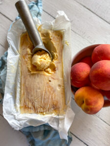 peach ice cream being scooped and a bowl of peaches