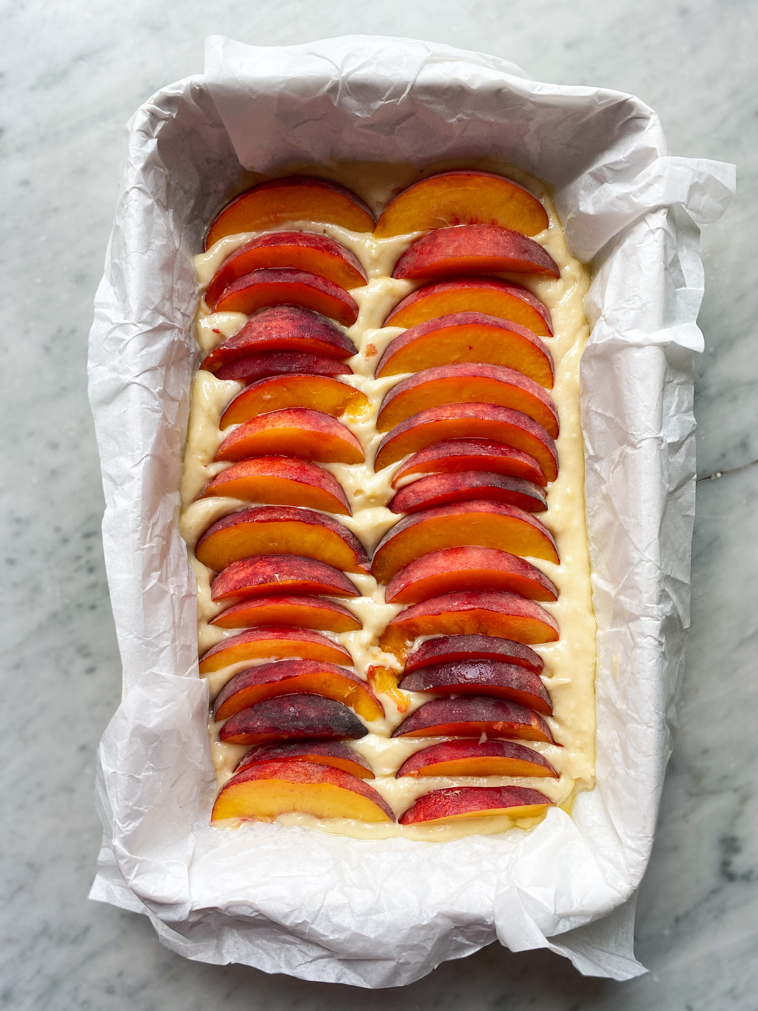 cake batter in parchment in a pan with sliced peaches on top
