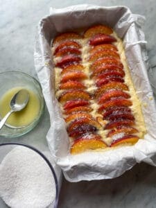 cake batter with sliced peaches on top with lemon and butter and sugar on top