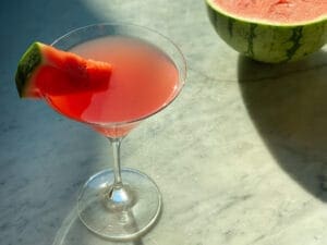 watermelon martini with a watermelon wedge and a watermelon in the backround