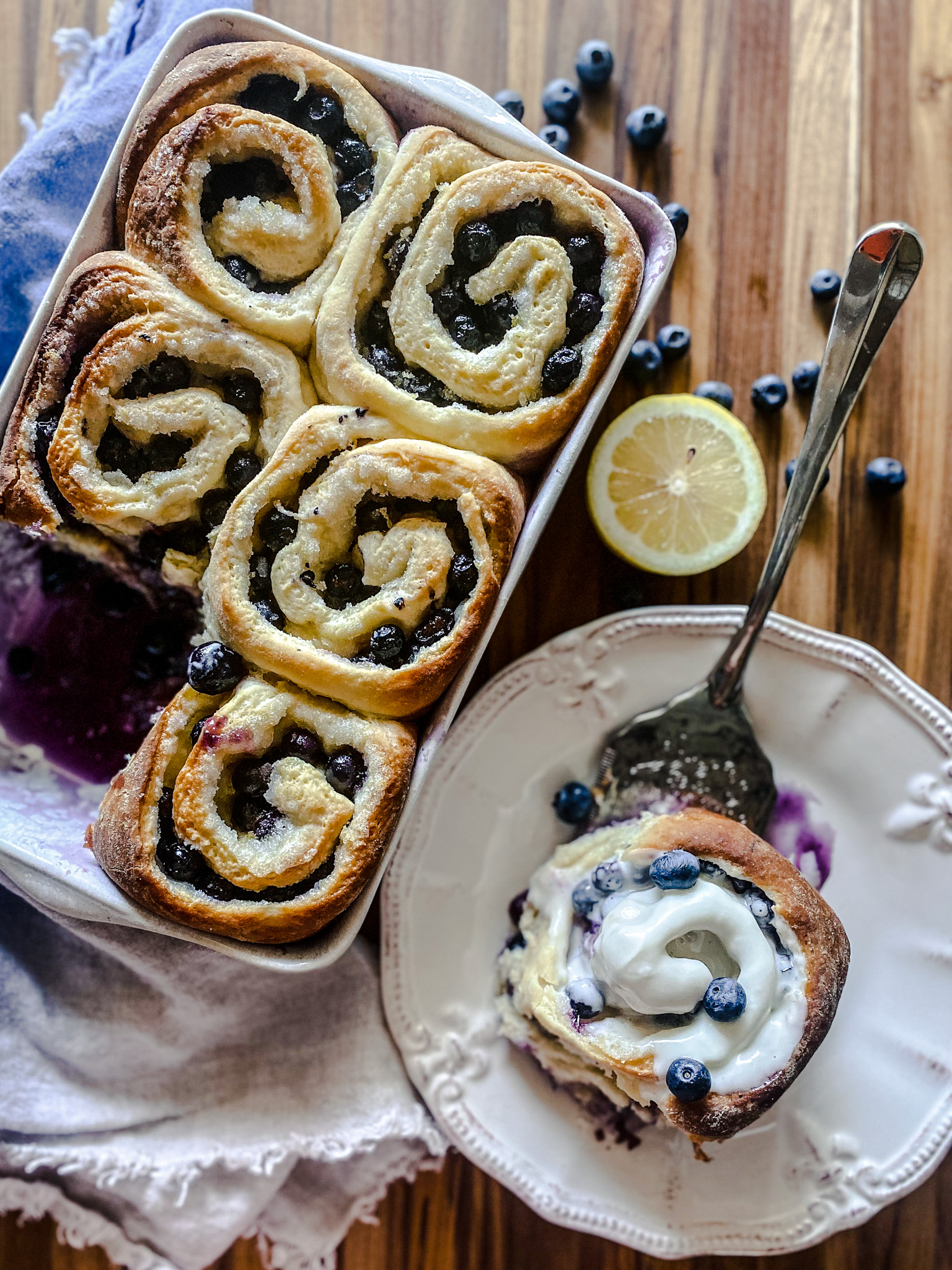 blueberry sweet rolls with one served on a plate with frosting and lemons and blueberries