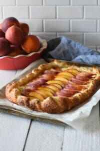 Cream cheese peach galette with a red pie pate of peaches and a blue napkin