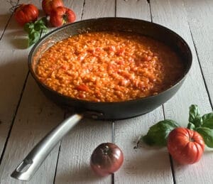 Tomato risotto in a pan with tomatoes and basil on the side
