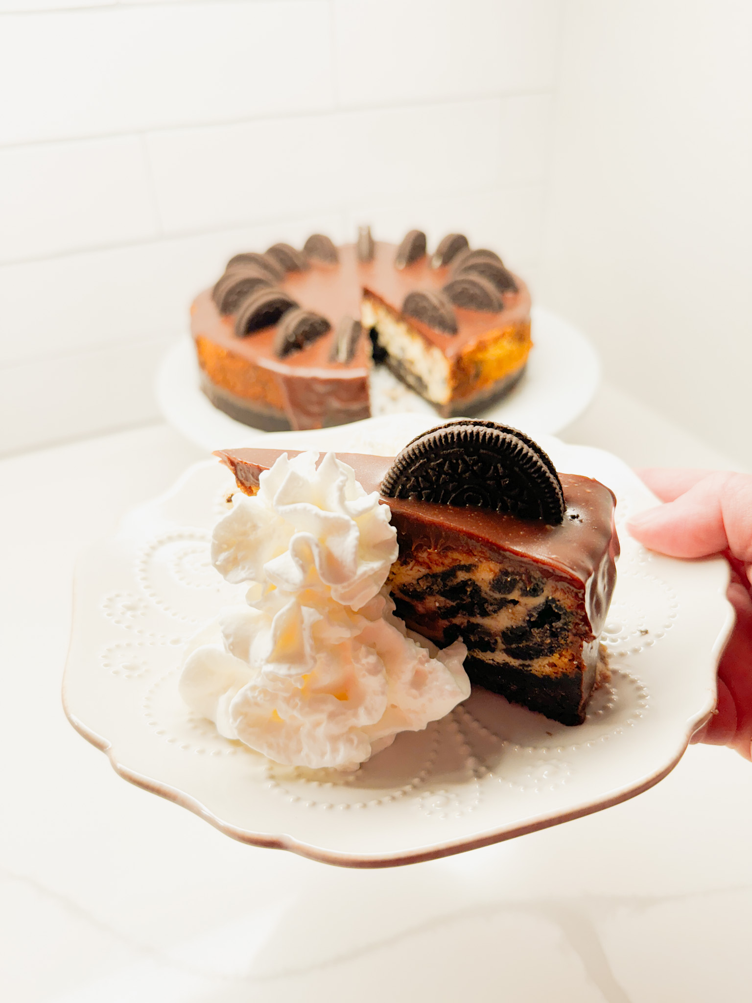 hand holding a slice of oreo cheese cake with the cheesecake in the background