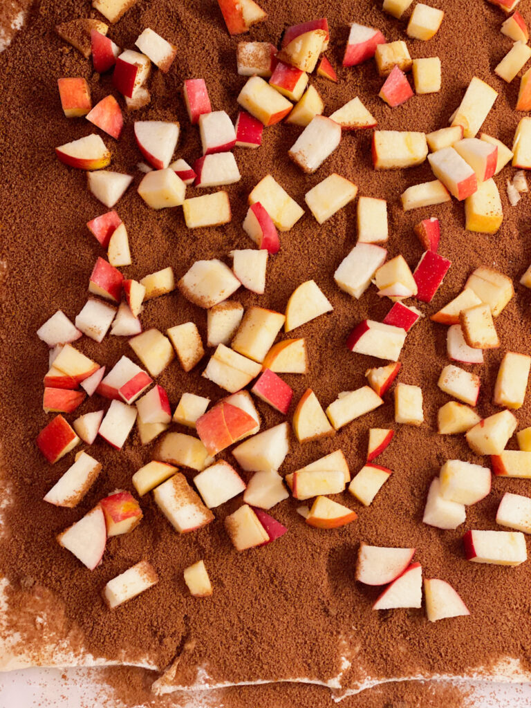 chopped red apple on cinnamon roll dough with cinnamon