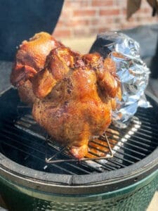 3 chickens standing up on a grill, one has foil on it