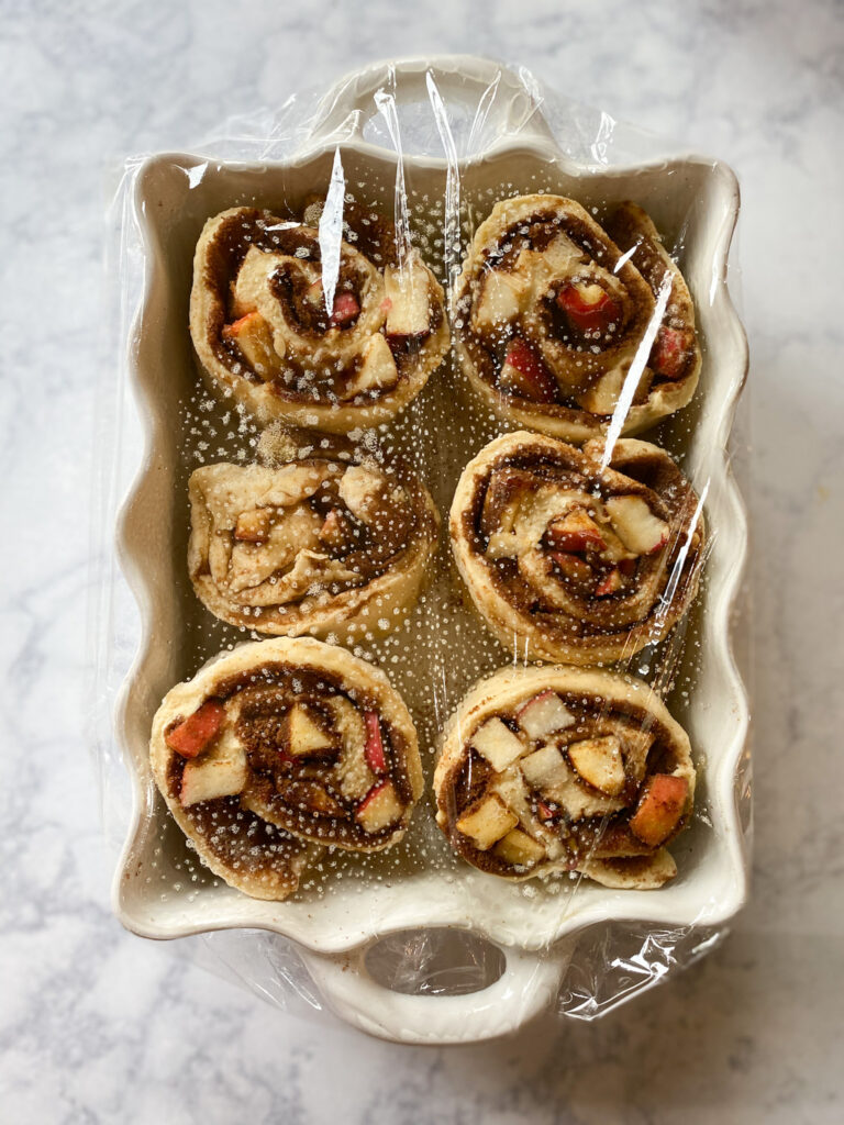 apple cinnamon rolls covered in plastic wrap