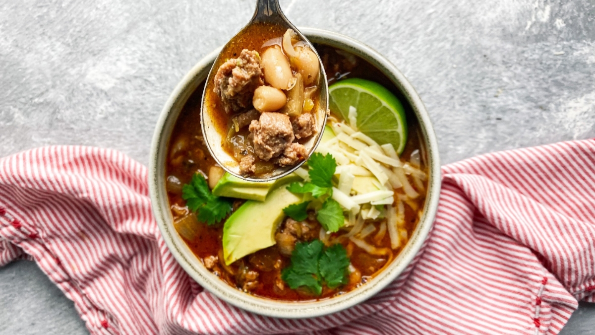 White Turkey chili in a bowl with lime and avocado and cilantro and cheese with a spoon of the soup