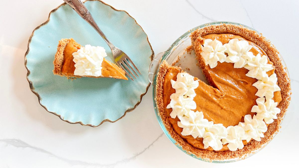 Pumpkin chifon pie with whipped cream and a slice cut out on a blue plate