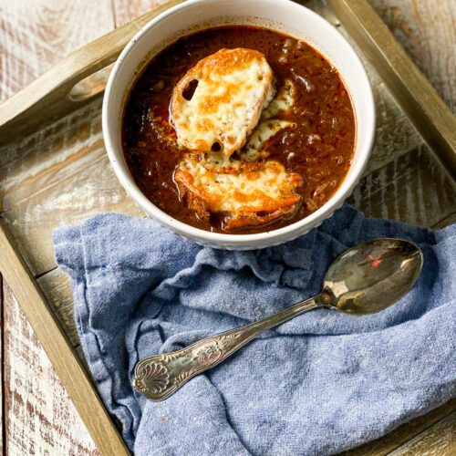 onion soup in a bowl with a cheese covered piece of toast and a blue napkin