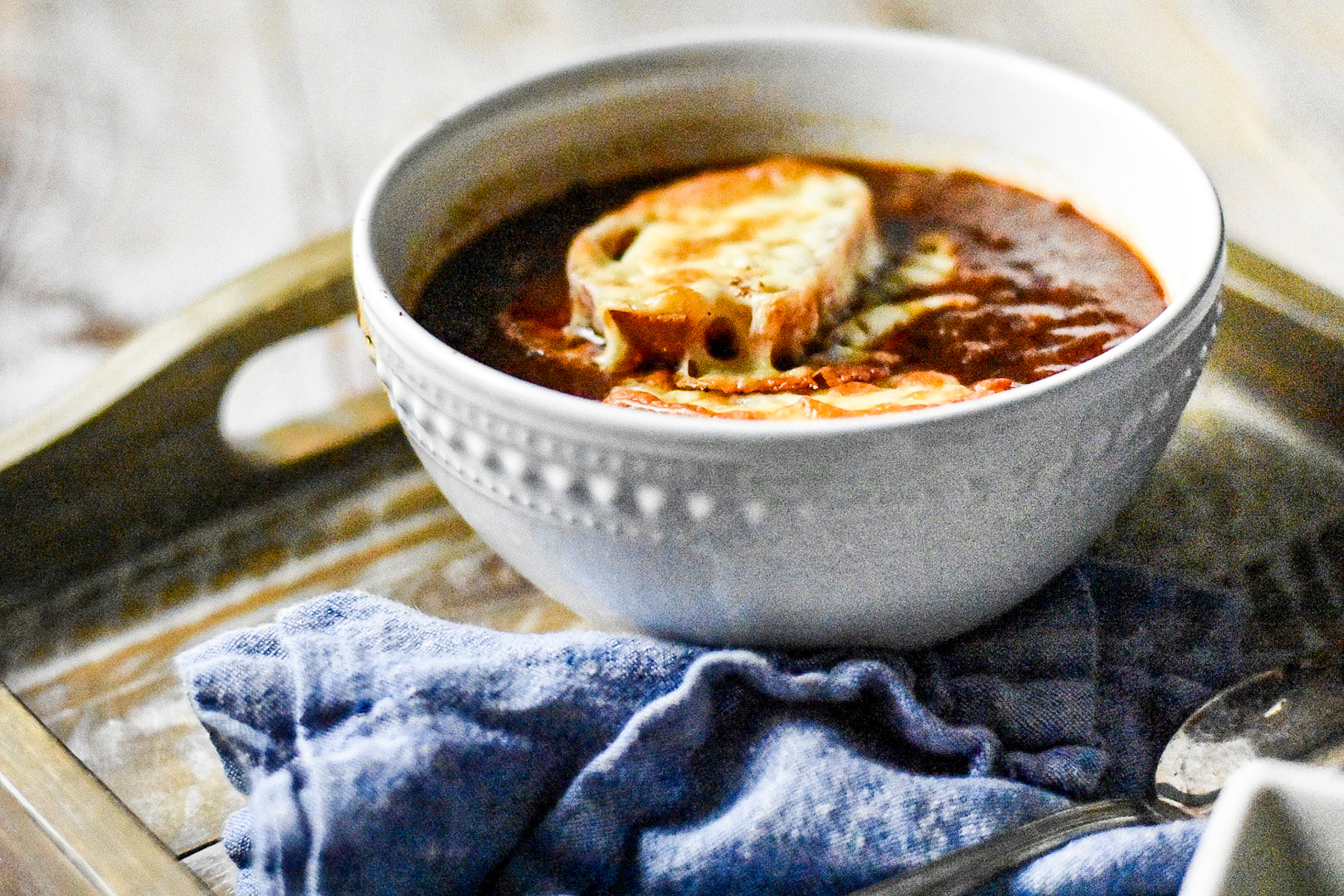 onion soup in a bowl with a cheese covered piece of toast and a blue napkin