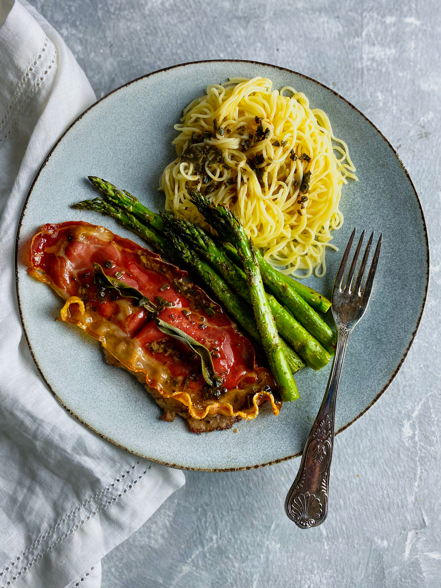 veal saltimboca on a plate with angel hair pasta and asparagus